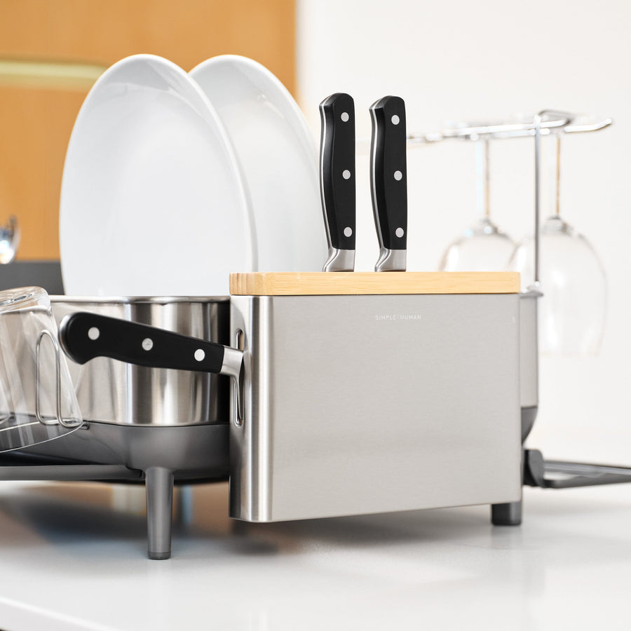 Detail view of Simplehuman Brushed Steel Knife Block with Bamboo top, shown securely holding knives next to dishware.