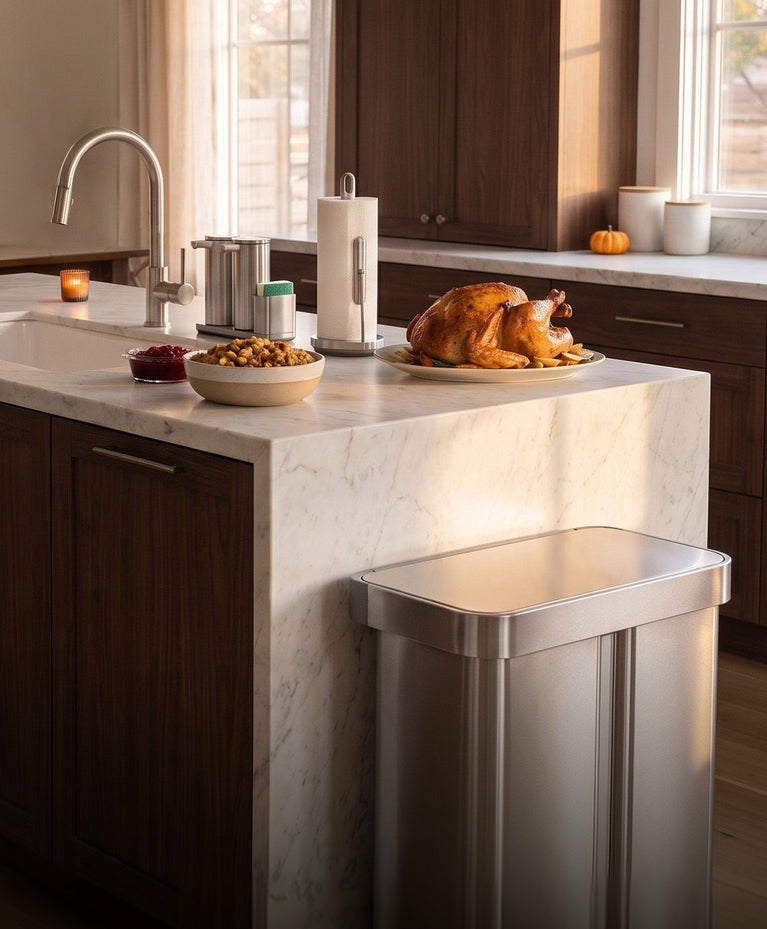Roasted turkey and side dishes on a Thanksgiving kitchen island, with a Simplehuman Sensor Pump Duo, Paper Towel Holder with Spray, and stainless steel step recycler.