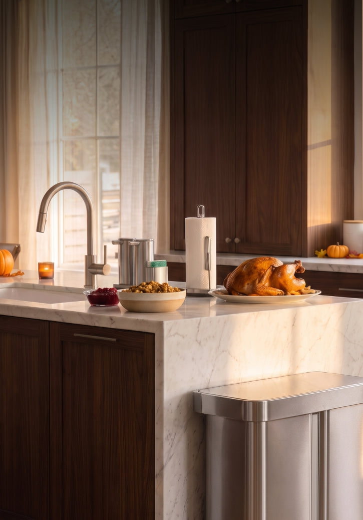 Roasted turkey and side dishes on a Thanksgiving kitchen island, with pumpkins, a stainless steel Simplehuman step recycler, Sensor Pump Duo, and Paper Towel Holder with Spray.